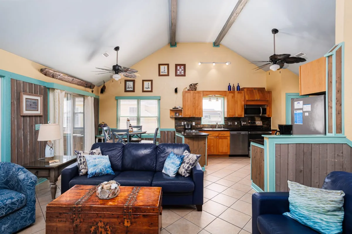 Una sala de estar con asientos azul oscuro y una mesa de centro de madera junto a la cocina.
