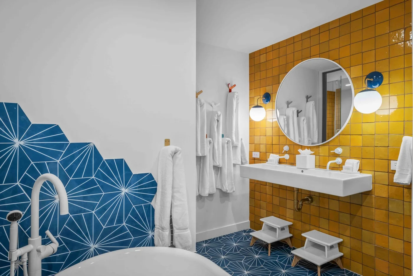 Un baño con un lavabo blanco frente a una pared de azulejos amarillos.