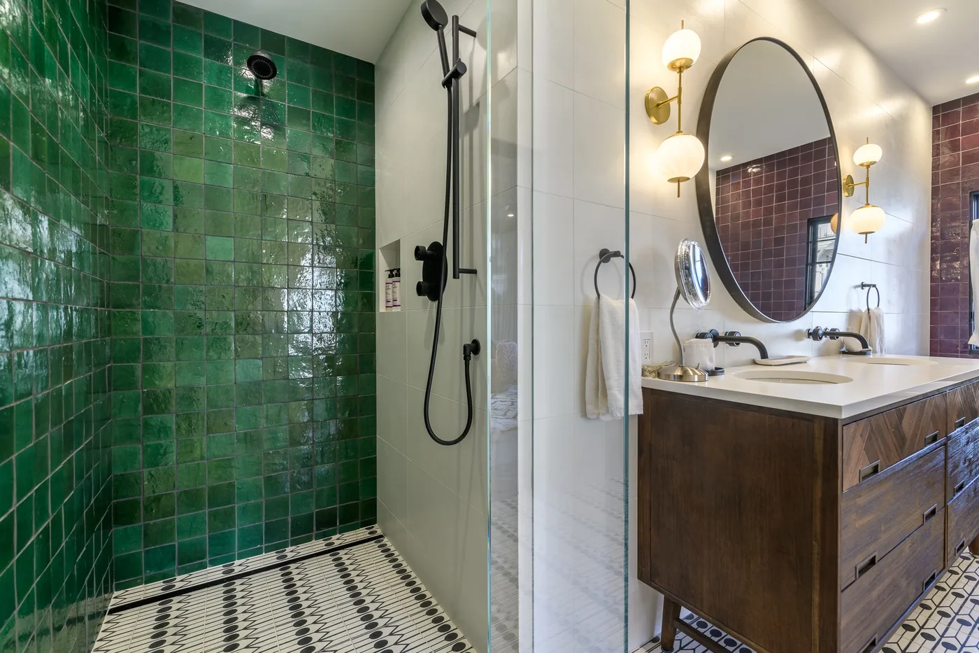 Un baño con una ducha de azulejos verdes y un tocador bajo un espejo redondo.