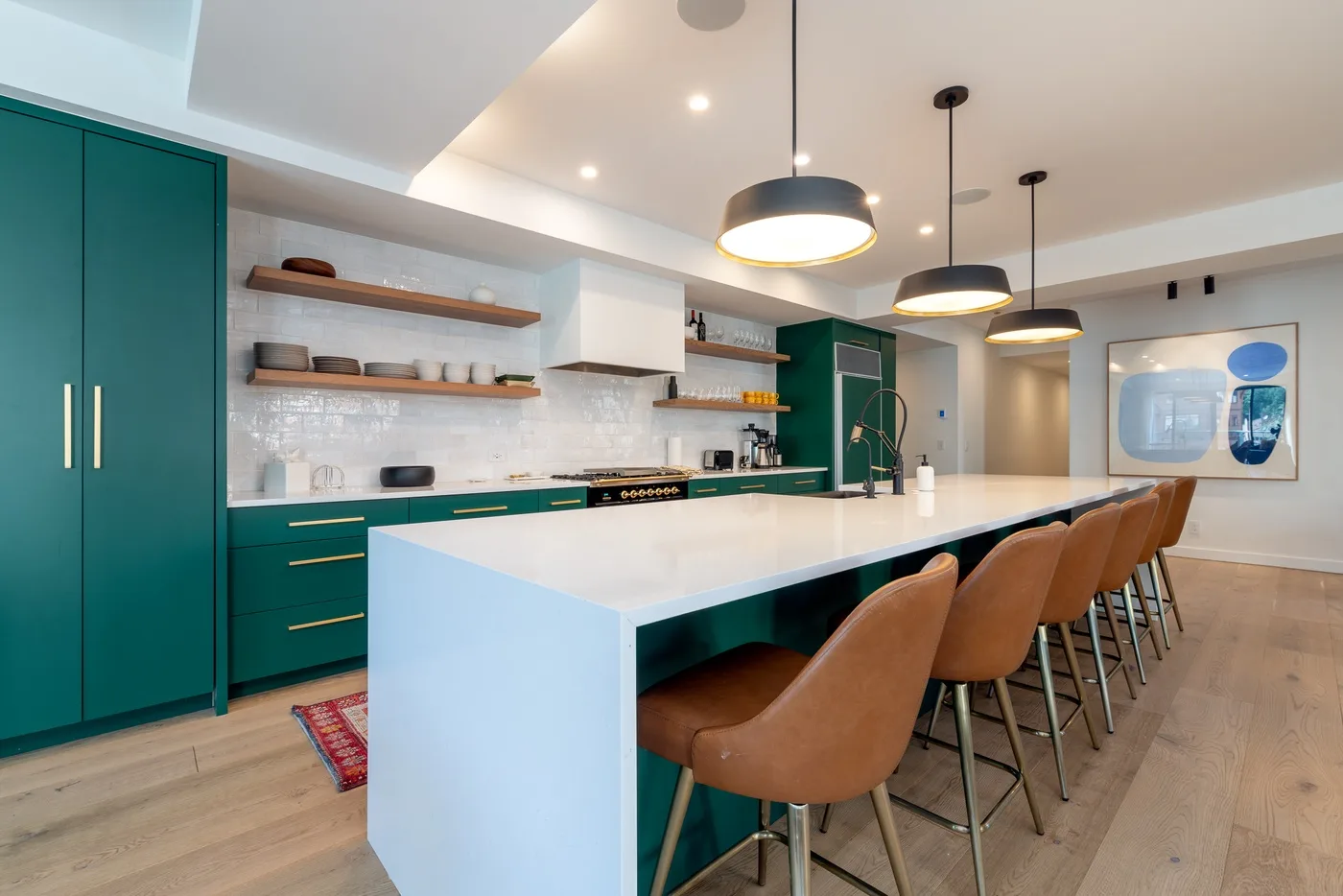 A modern kitchen with a long island, brown seating, and pendant lights.