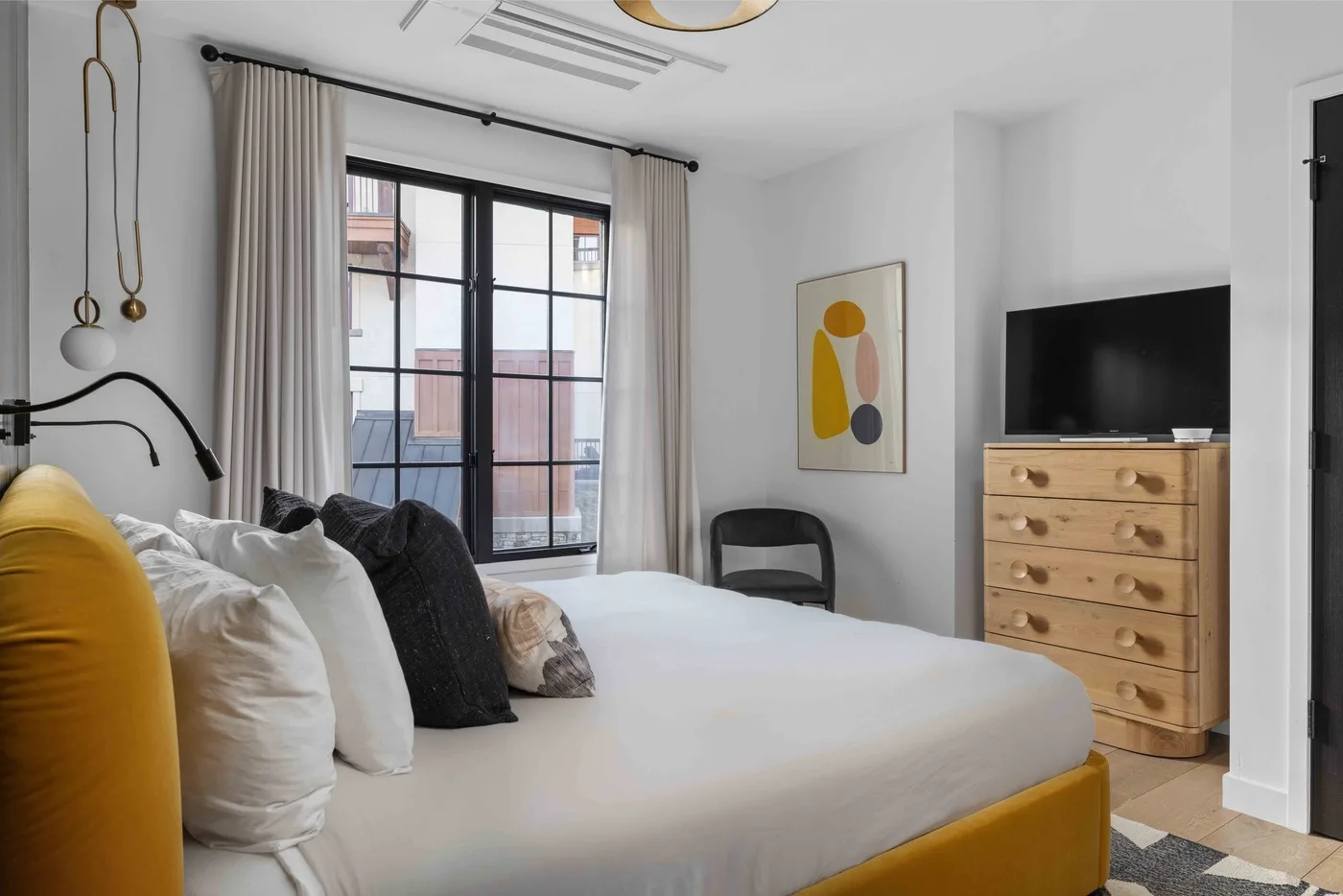 Dormitorio con cama, una ventana grande y televisor sobre una cómoda.
