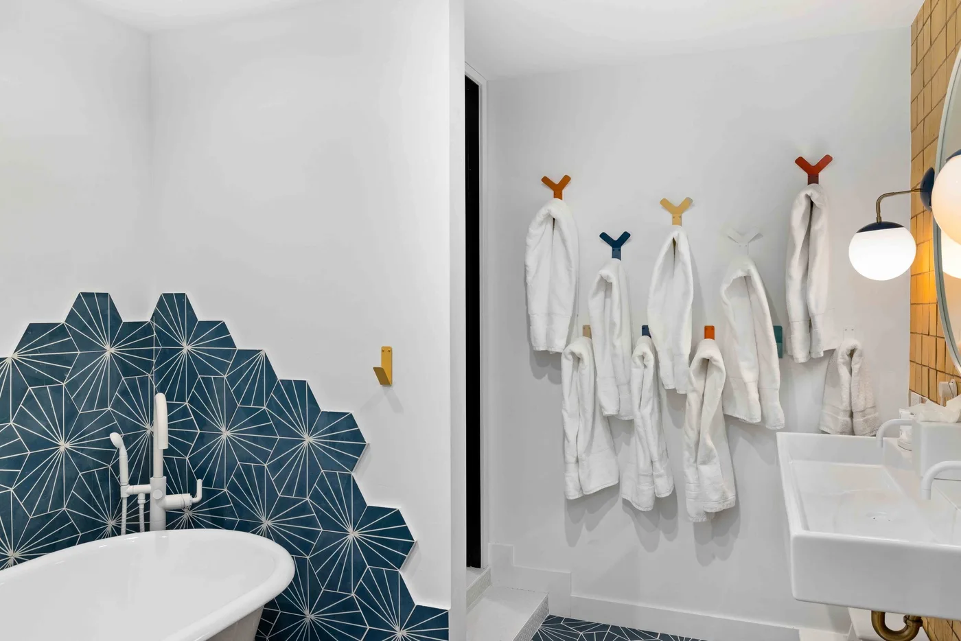Un baño luminoso con bañera, azulejos estampados y albornoces colgados en ganchos.