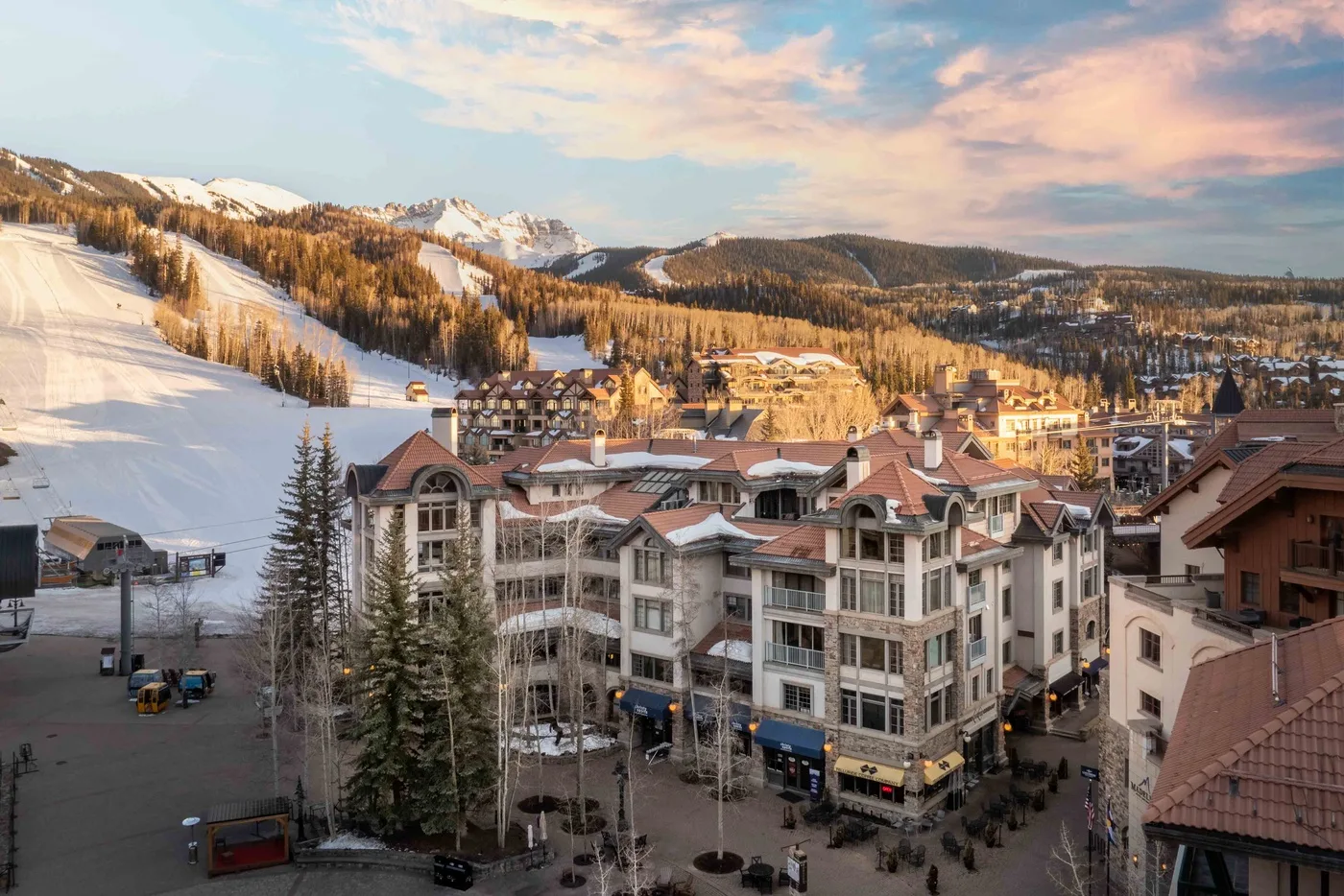 Un pueblo turístico de montaña se encuentra junto a pistas nevadas bajo un cielo colorido.