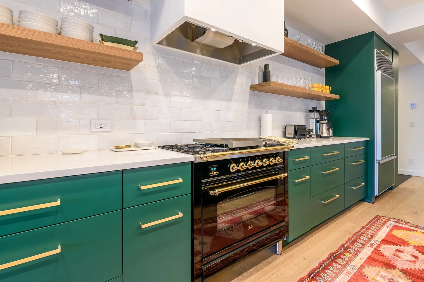 Una cocina moderna con gabinetes verdes, una estufa amplia y estantes de madera abiertos.