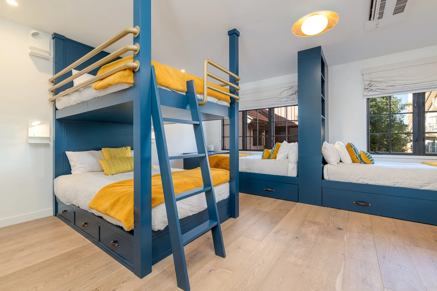 Un dormitorio luminoso con literas azules y asientos junto a las ventanas.