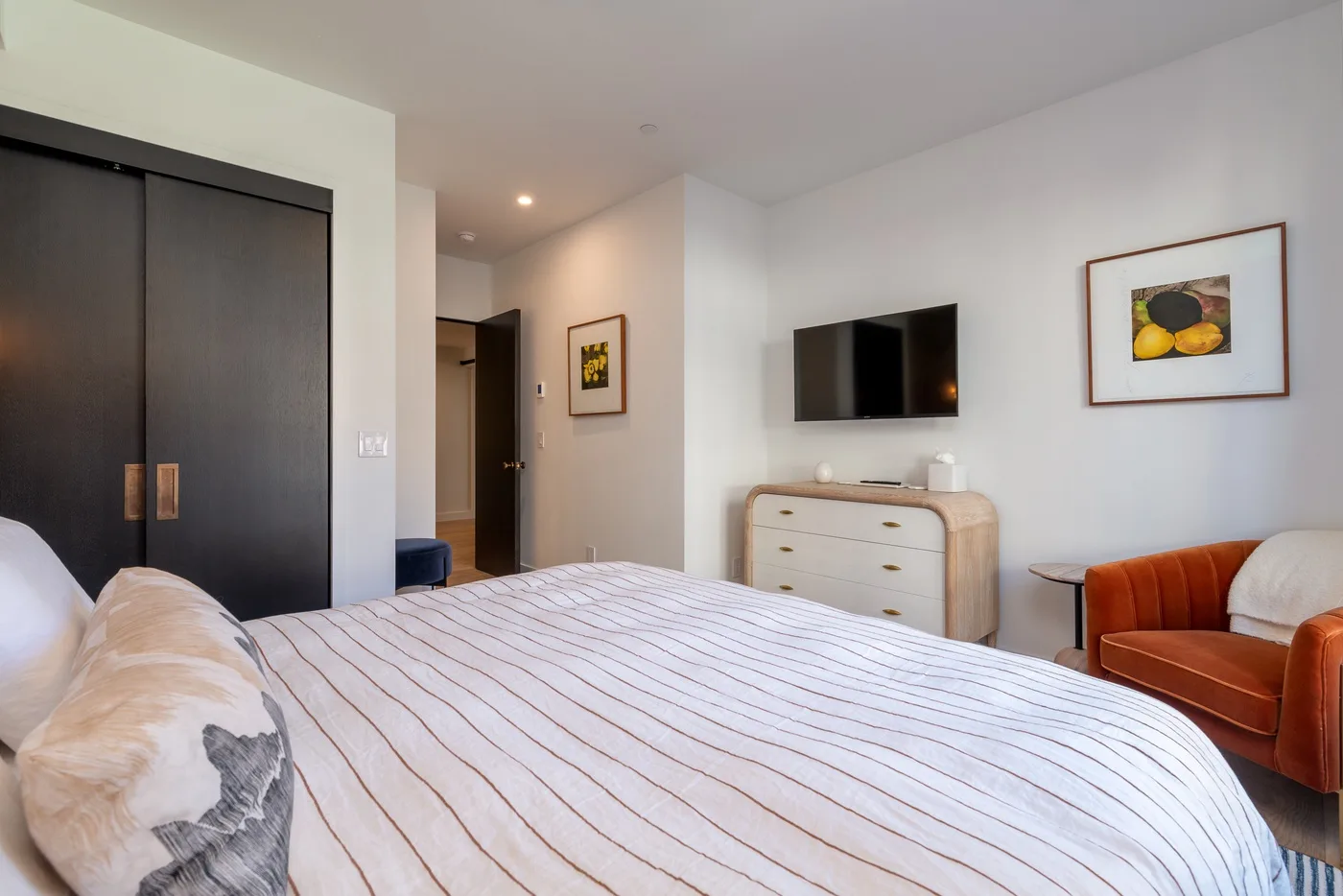 Un dormitorio con cama, armario oscuro, cómoda y televisor montado en la pared.