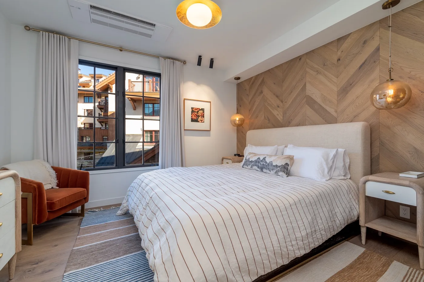 Dormitorio con una cama bien arreglada, un sillón y grandes ventanas.