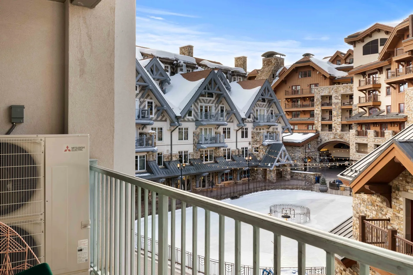 Un balcón da a un patio cubierto de nieve, rodeado de edificios de estilo alpino.