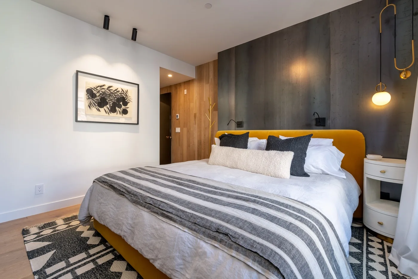 Un dormitorio moderno con una cama vestida de blanco y una manta a rayas.