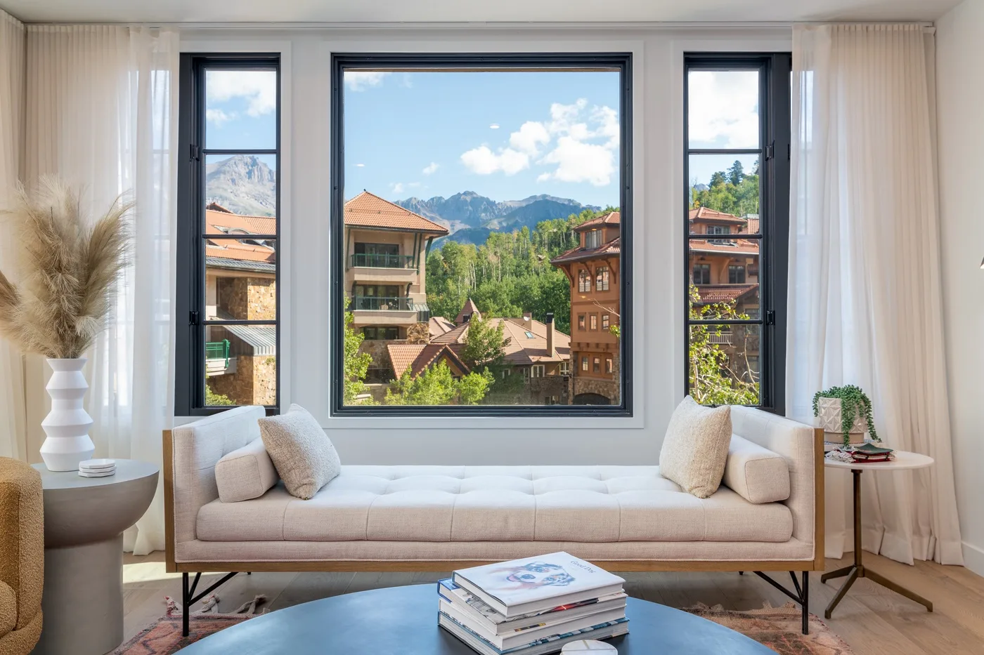 Una sala luminosa con asientos acolchados frente a grandes ventanas y vistas a las montañas.