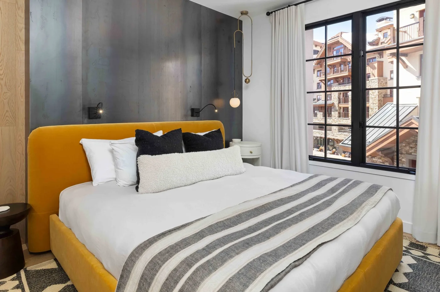 Dormitorio con una cama, cabecero color mostaza y una ventana grande.