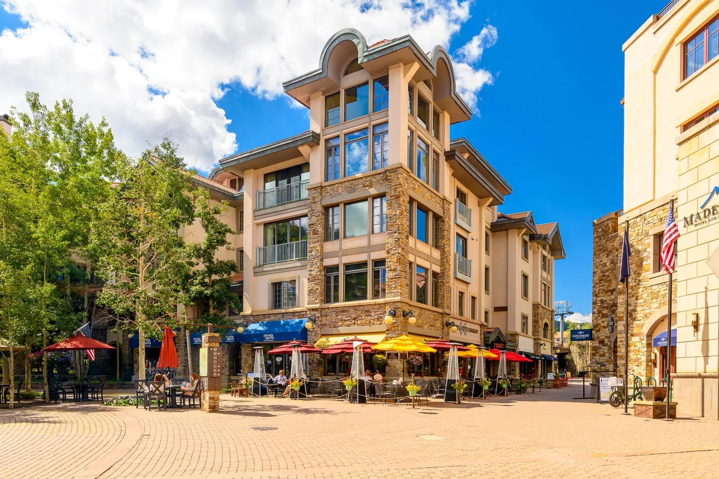 A multi-story building with outdoor dining seating along a paved plaza.