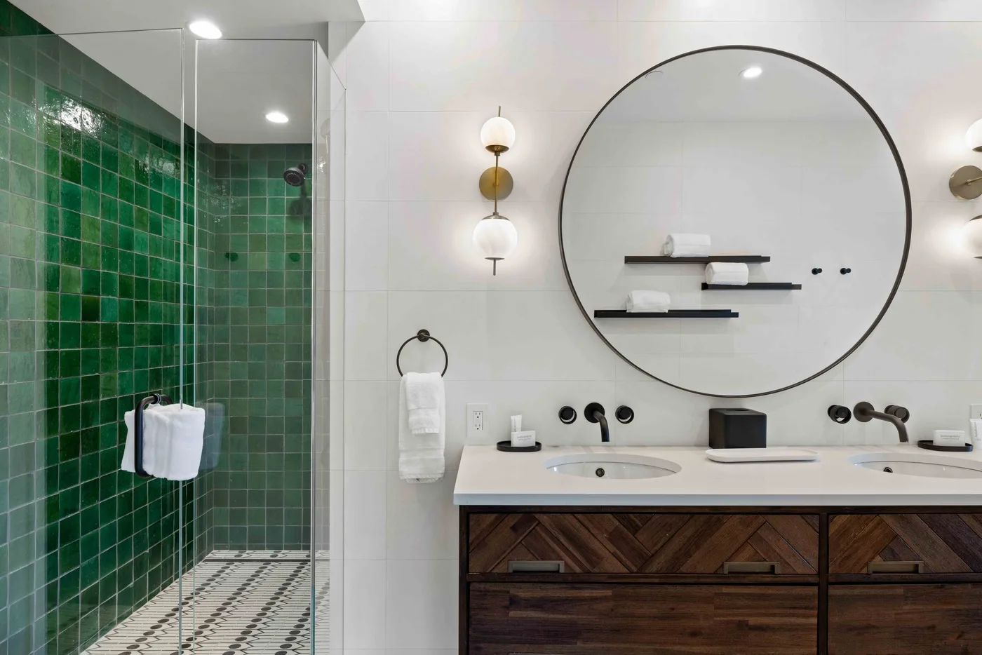 Un tocador de baño moderno con un gran espejo redondo junto a una ducha con azulejos verdes.