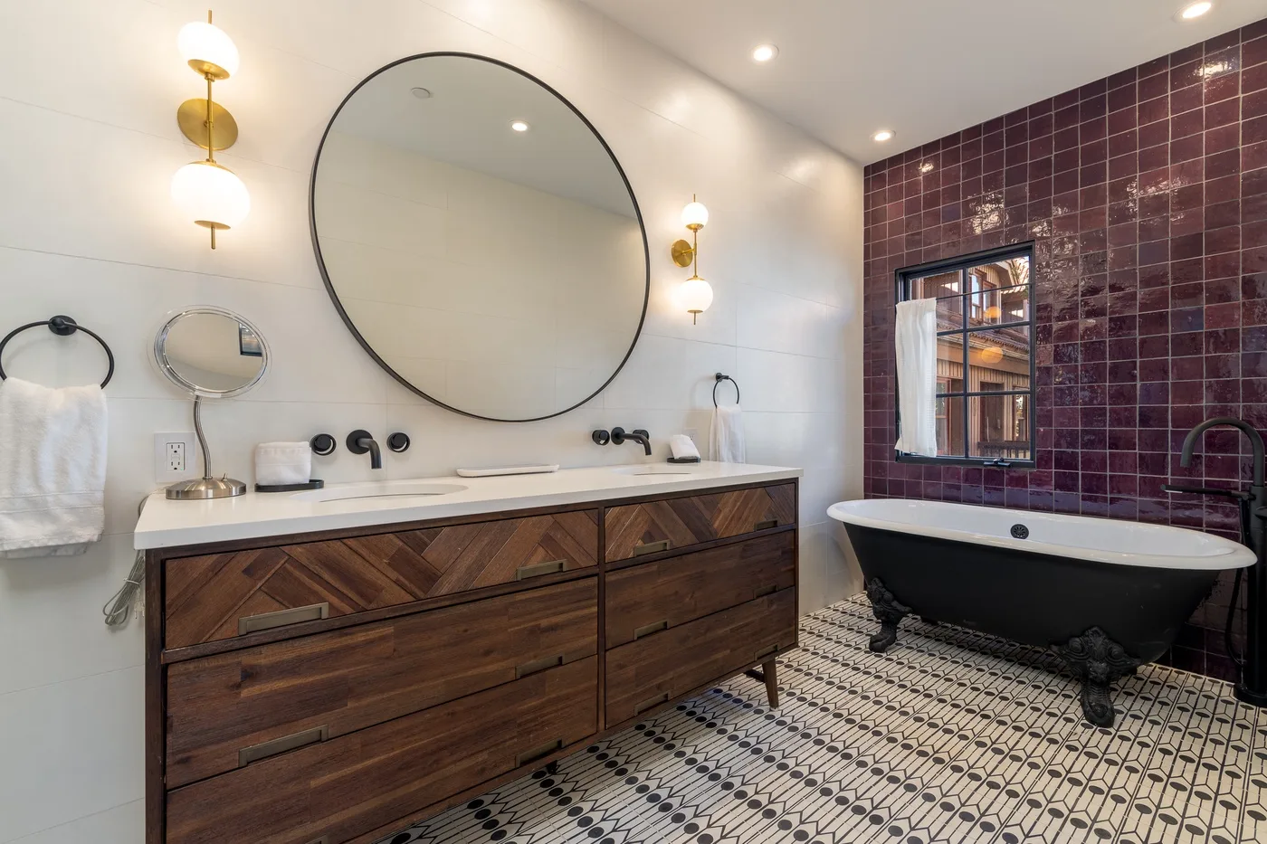 Un baño con un mueble de madera largo, un espejo redondo grande y una bañera exenta.