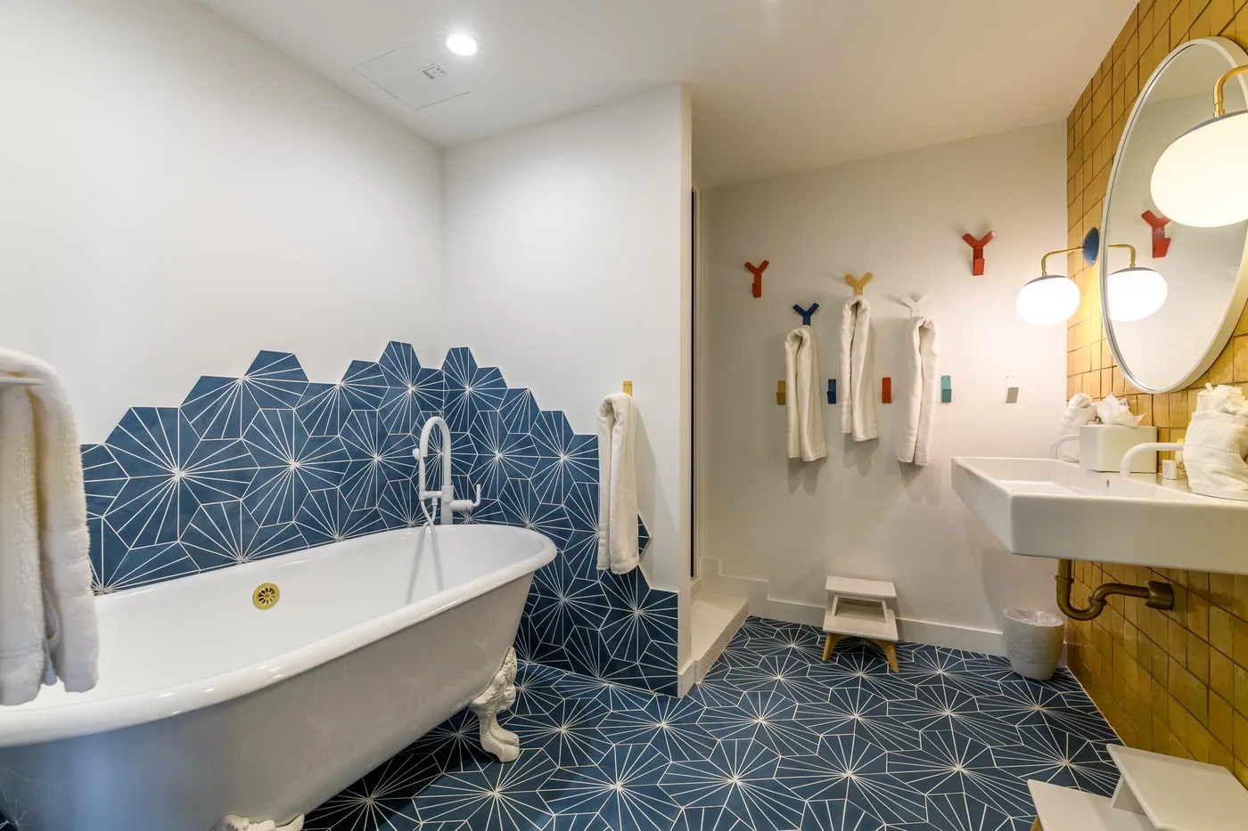 Un baño con bañera, azulejos azules estampados y un lavabo bajo un espejo redondo.