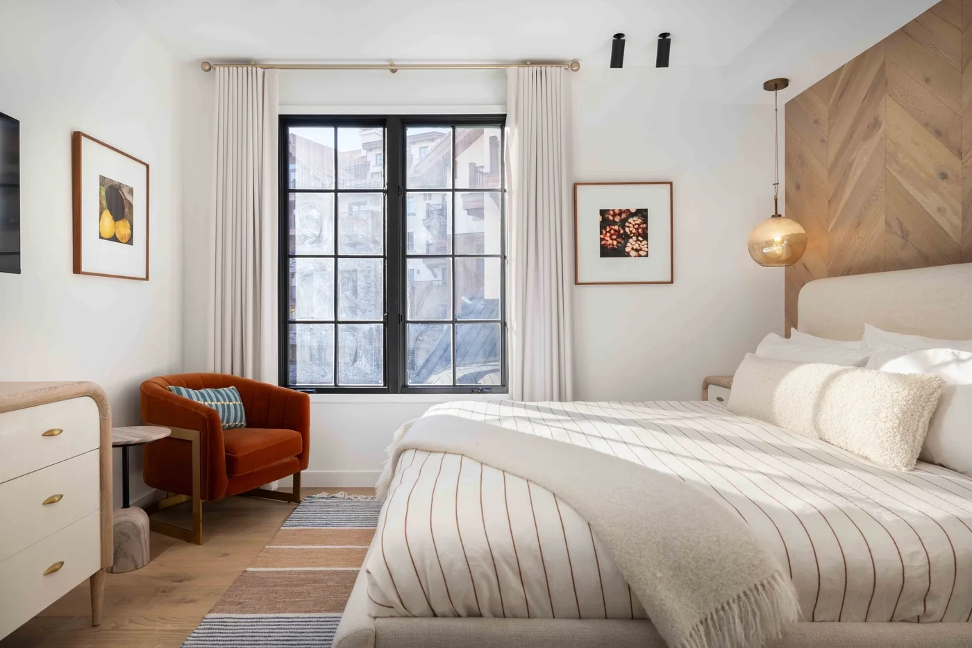 Un dormitorio luminoso con una ventana grande, una cama y un sillón tapizado.