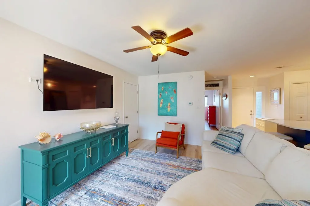 A bright living room with a teal cabinet, wall-mounted television, and seating.
