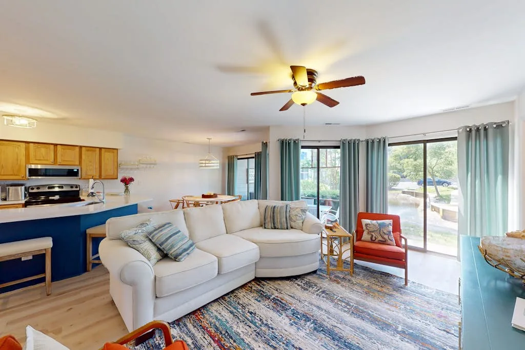 A bright living room with a sectional sofa, colorful rug, and large windows.