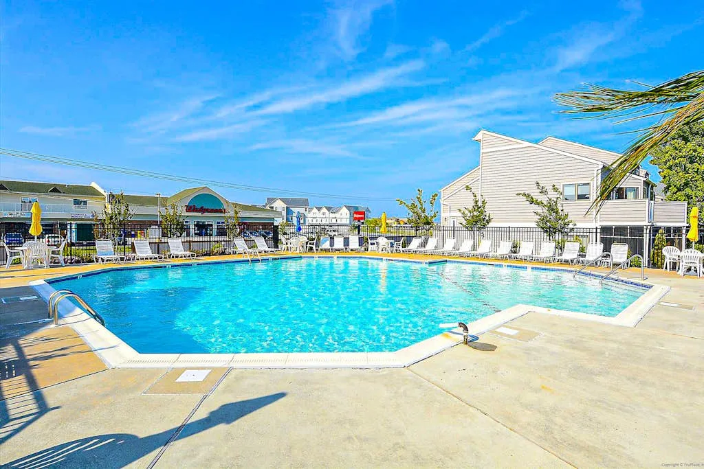 An outdoor swimming pool with lounge seating and buildings in the background.