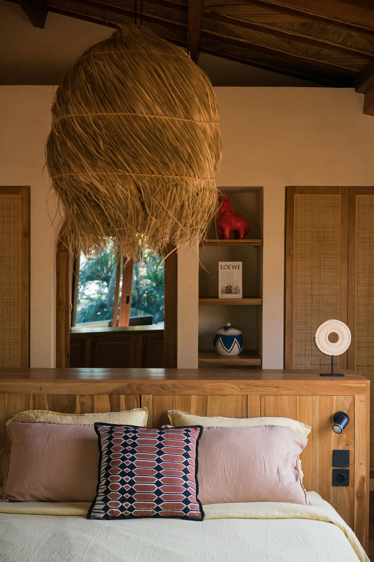 A bedroom with a bed beneath a large woven pendant light.