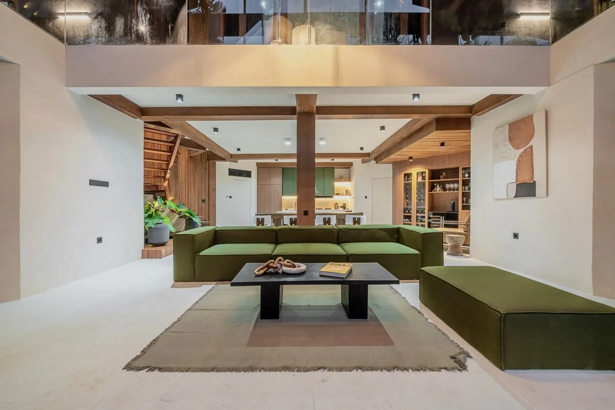 A spacious living room with green seating, a low table, and a rug.