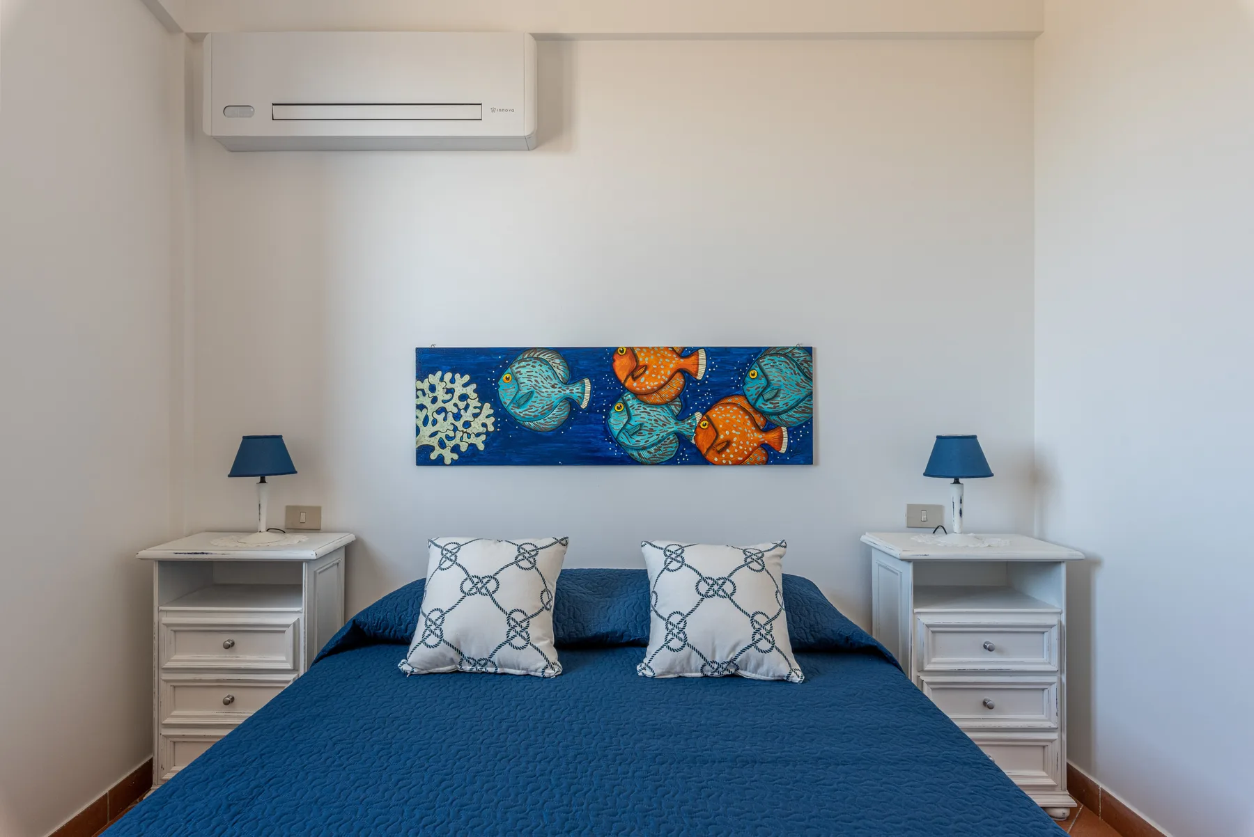 Un dormitorio con una cama azul, mesitas de noche y una colorida obra de arte sobre el cabecero.