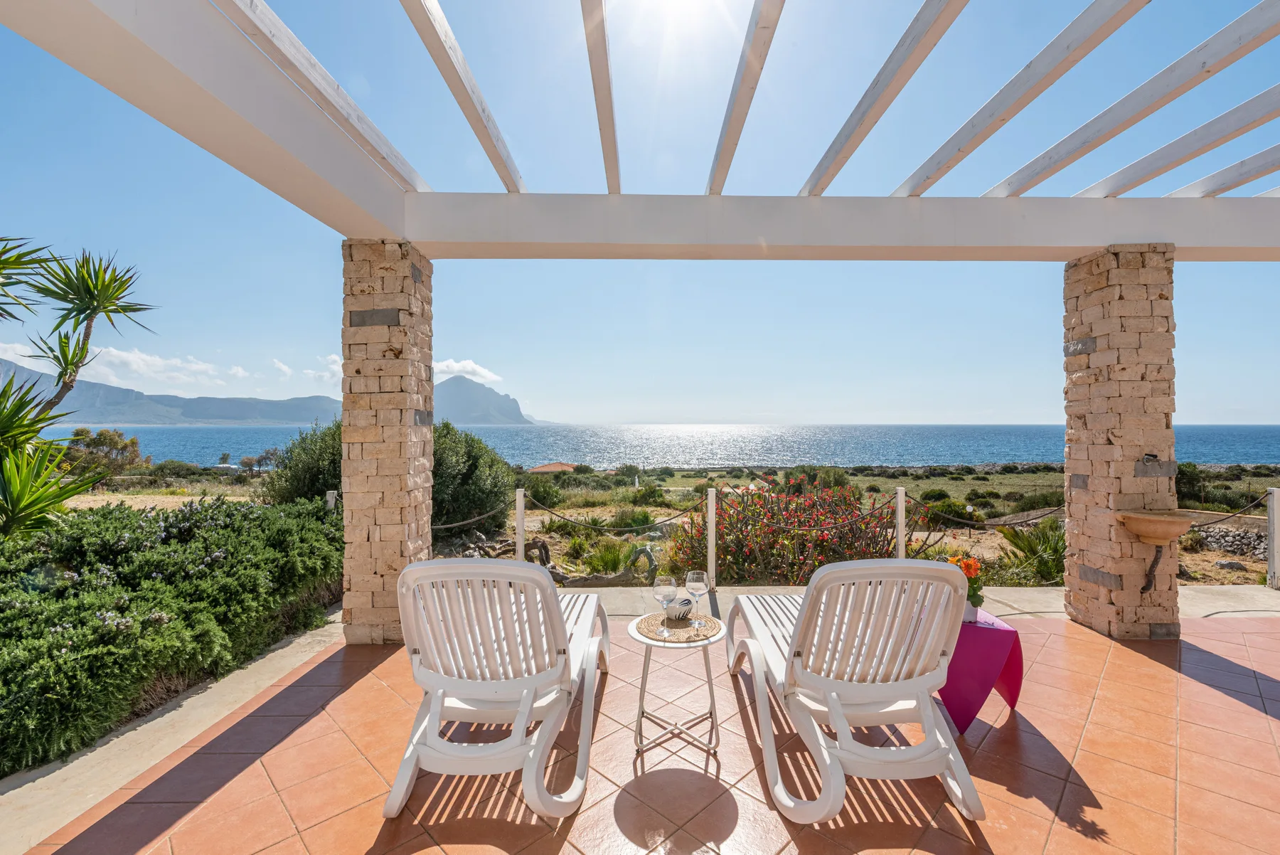 A covered outdoor terrace overlooks the sea, with seating and a small table.