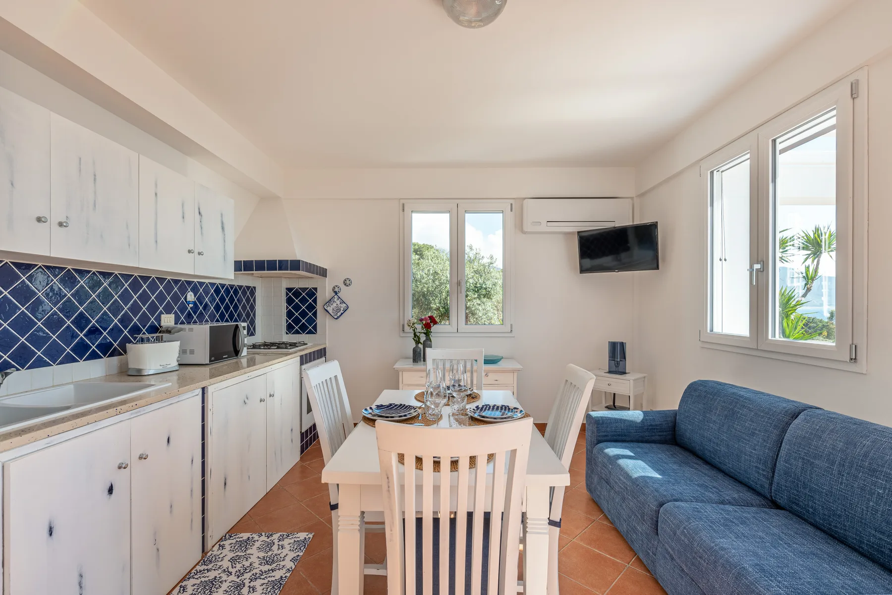 Una luminosa zona de comedor y cocina con un sofá azul junto a la mesa.