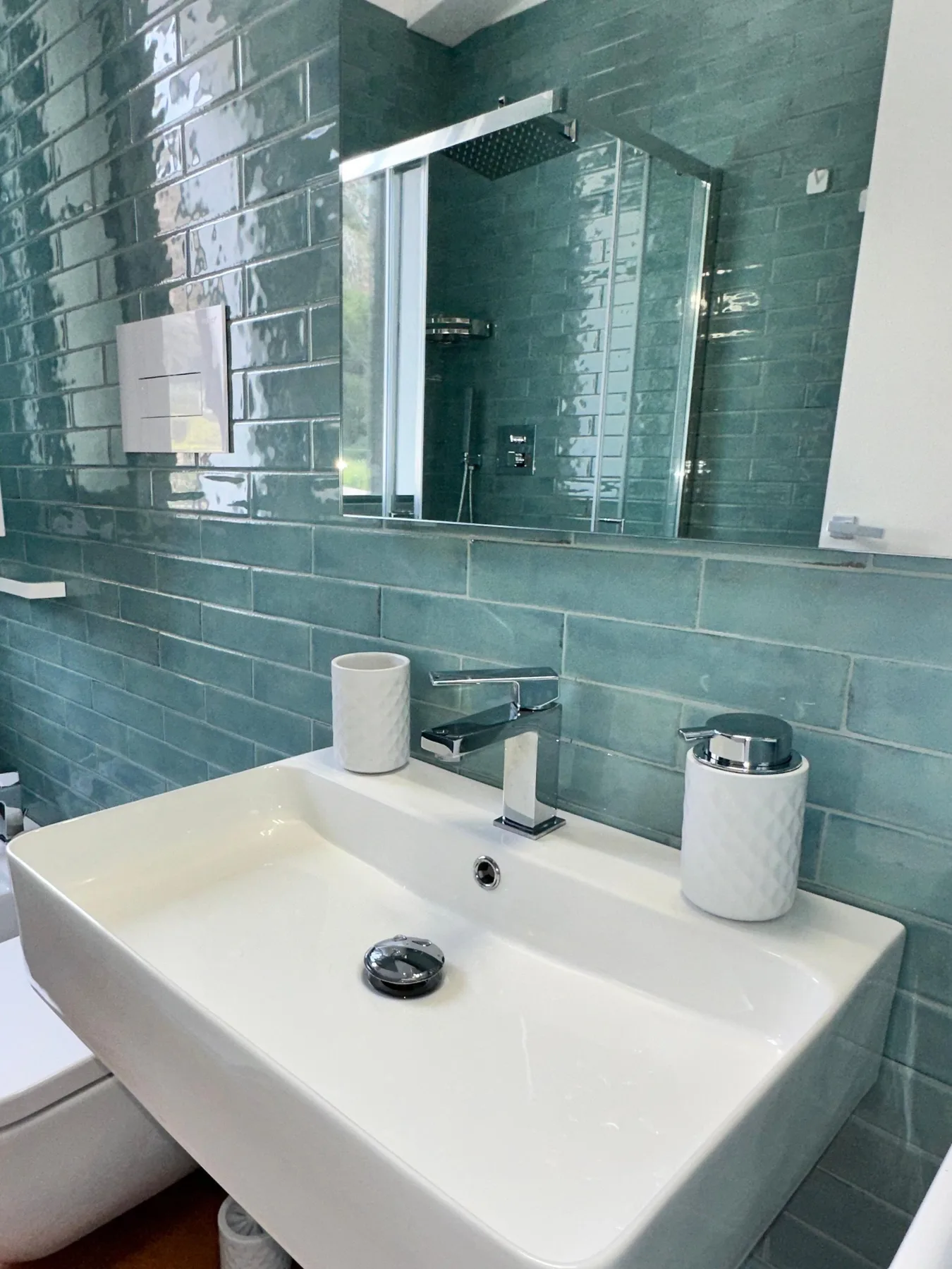Un lavabo de baño está bajo un espejo, con azulejos verdes en las paredes.