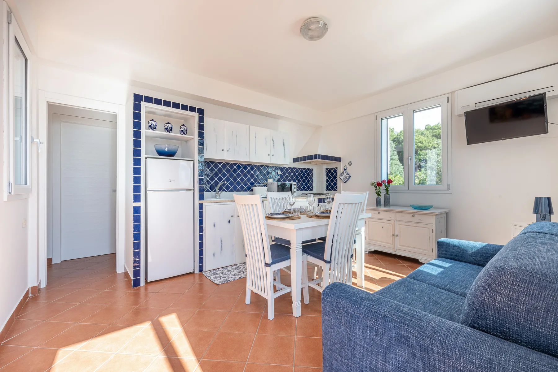 Una luminosa cocina y zona de comedor con armarios blancos y un sofá azul.