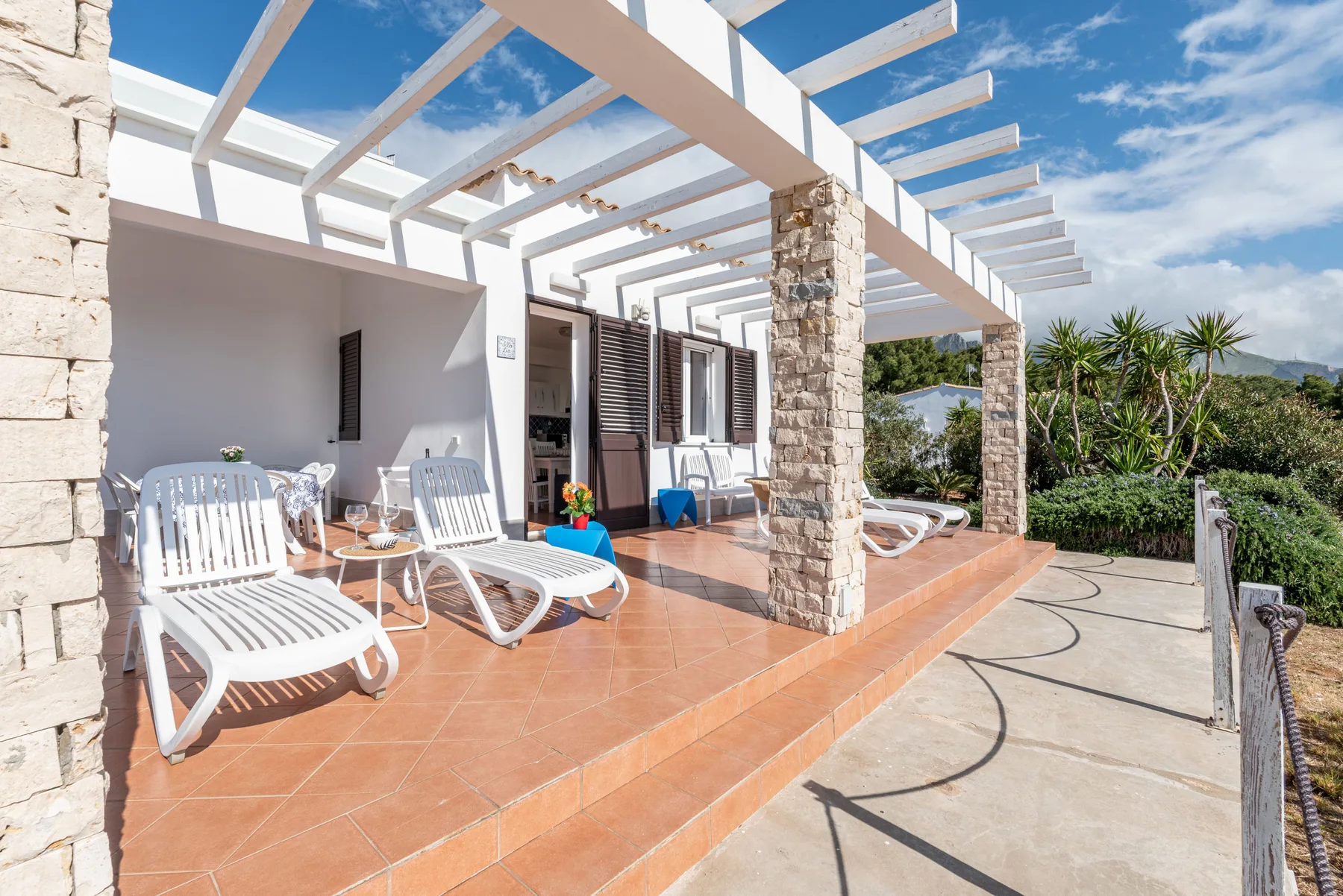 Un patio soleado con asientos blancos bajo una pérgola.