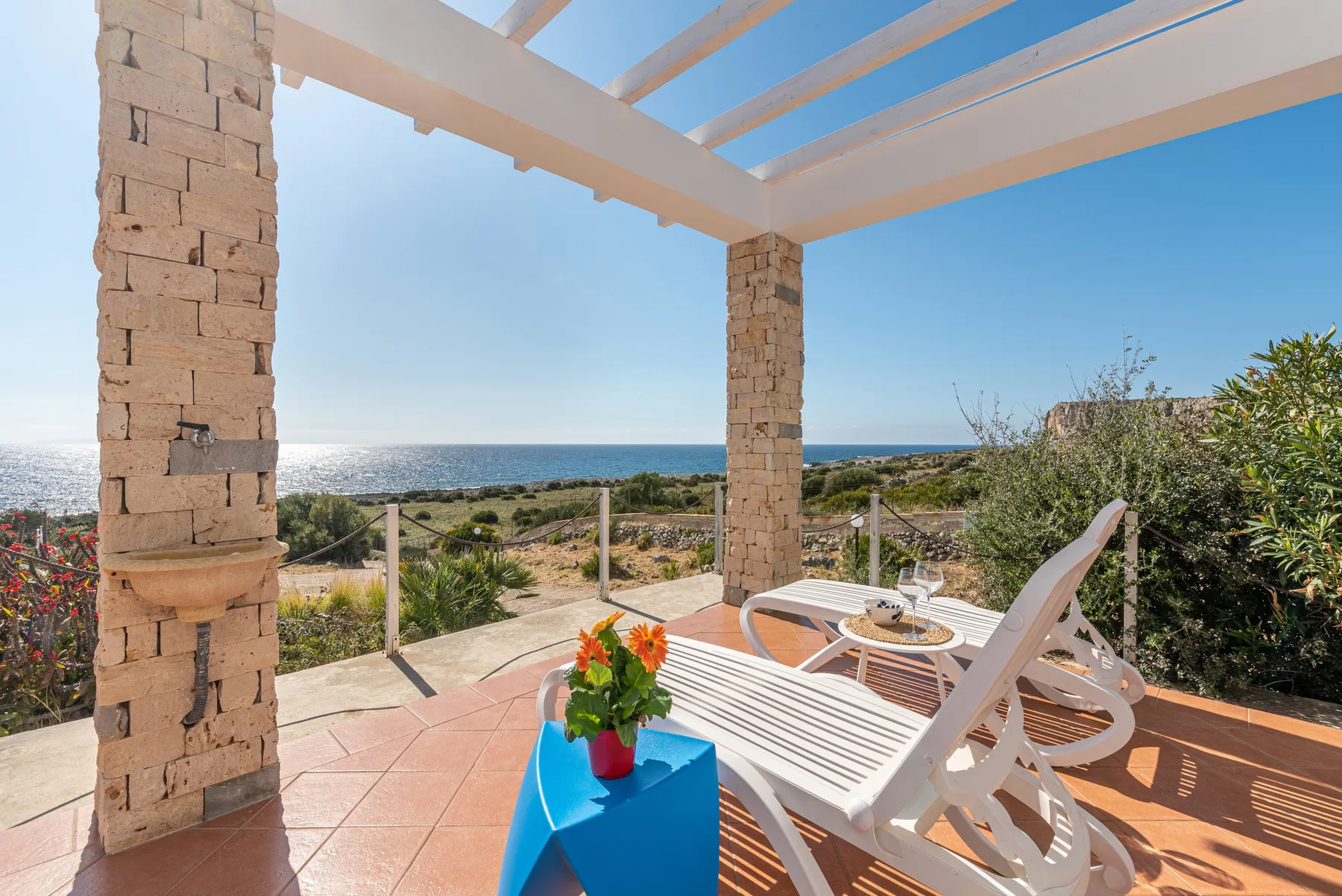 Un patio de baldosas con asientos blancos mira al mar bajo una pérgola.