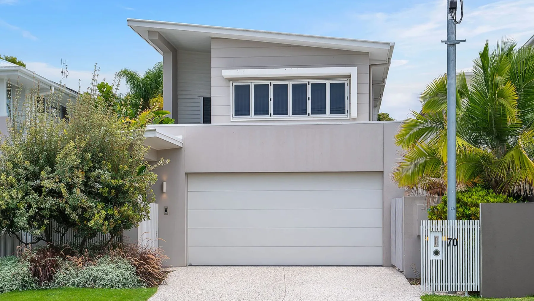 A modern house exterior with a wide garage door and landscaped plants.