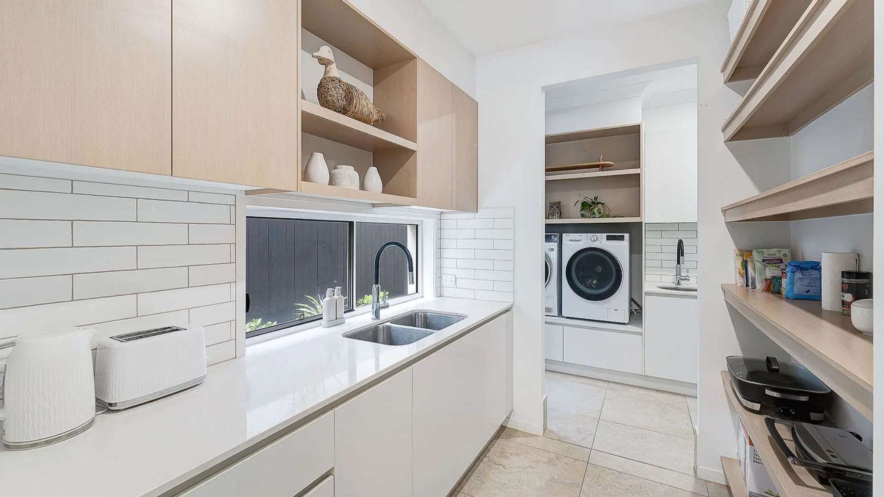 A bright laundry room with a sink, washer, and open shelving.