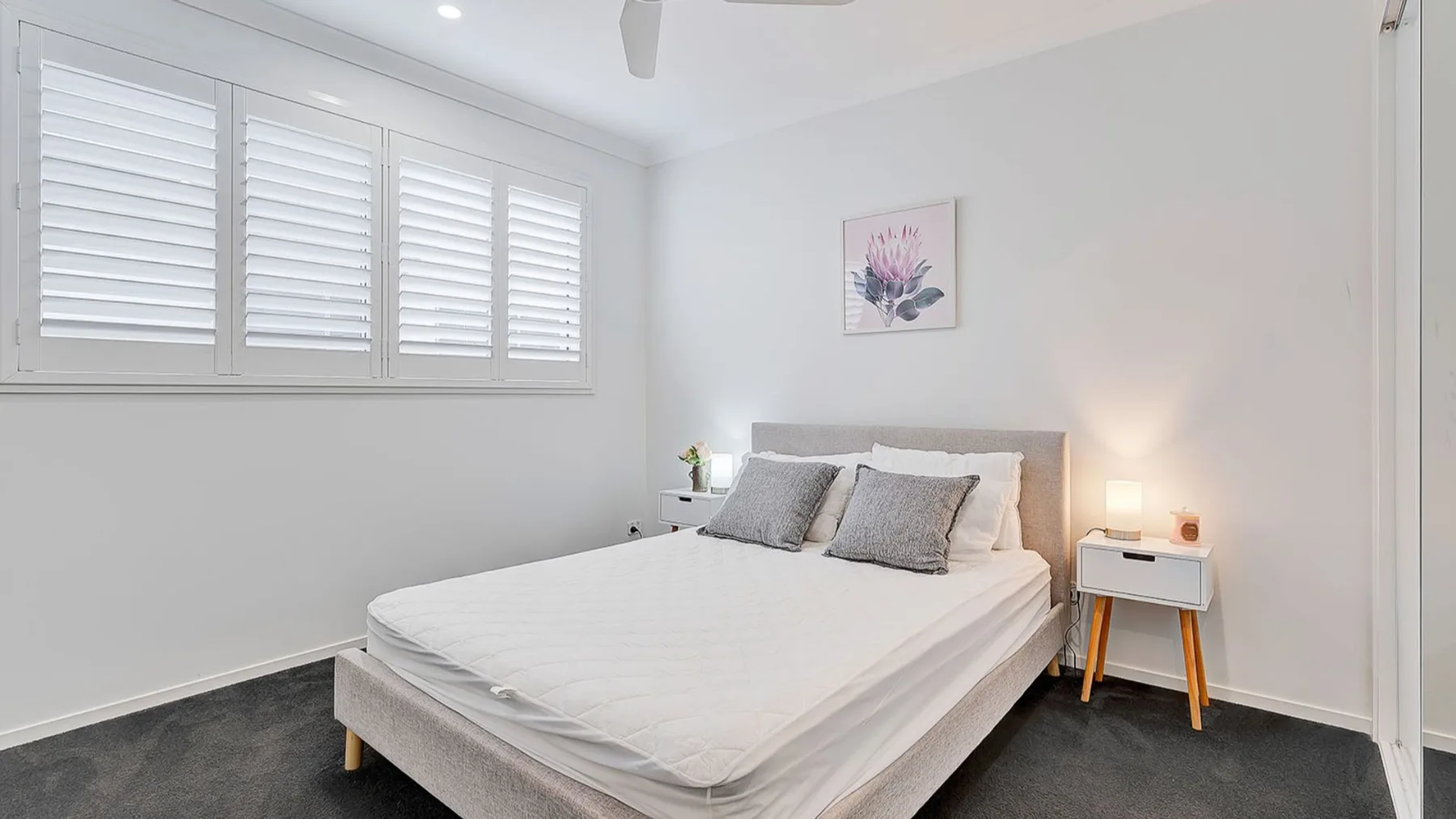 A bright bedroom with a neatly made bed beneath shuttered windows.