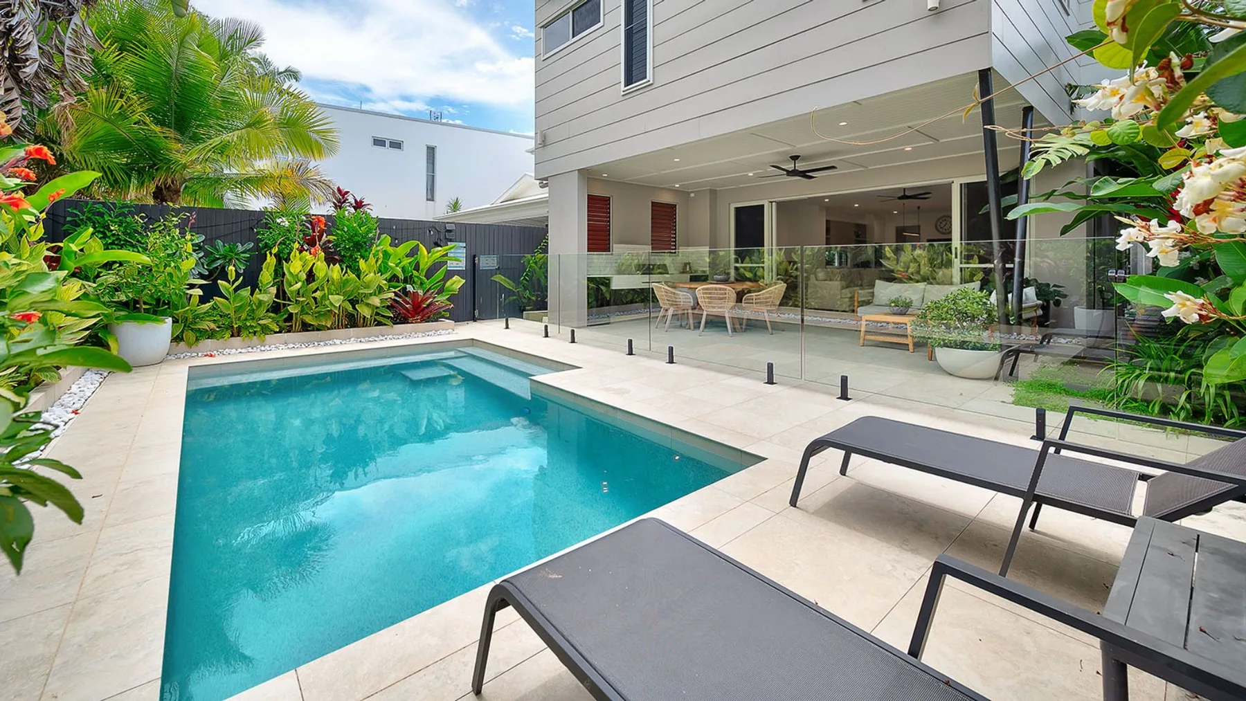 An outdoor pool beside a modern house, surrounded by tropical plants.