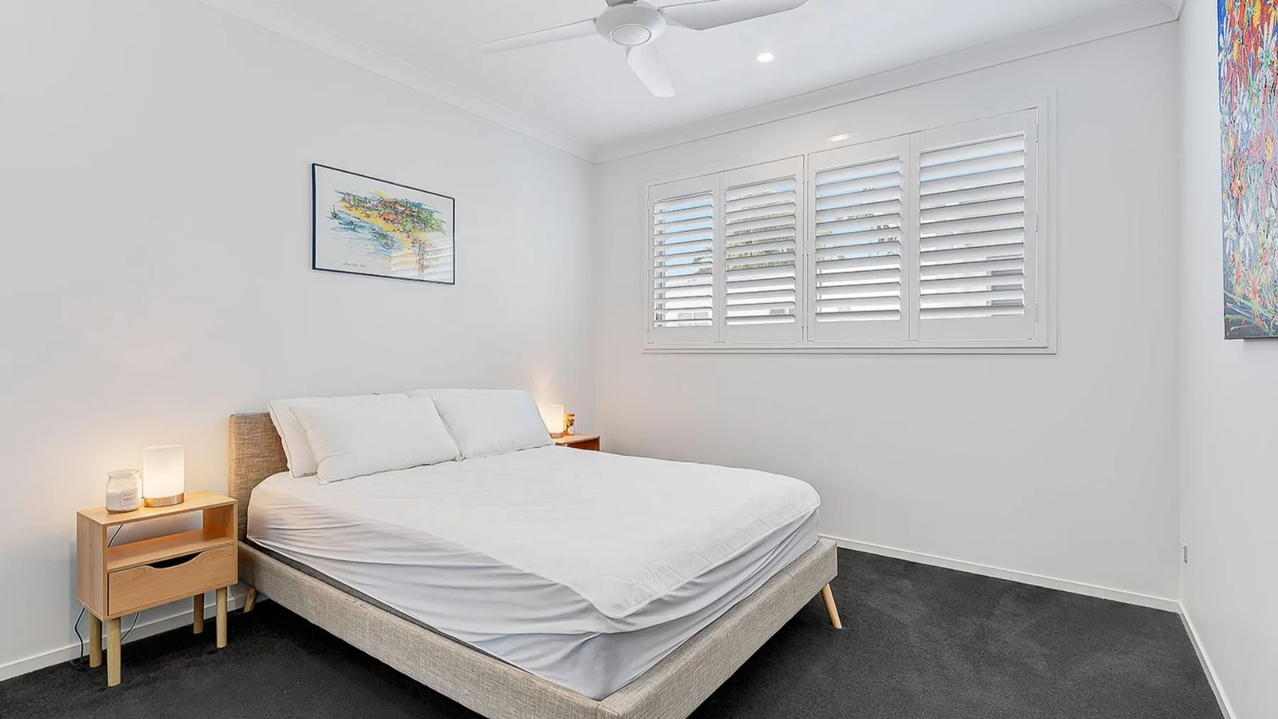 A bright bedroom with a bed beneath shuttered windows.