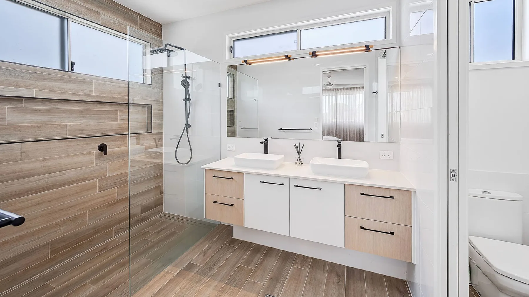 A bright bathroom with a double vanity and glass shower.