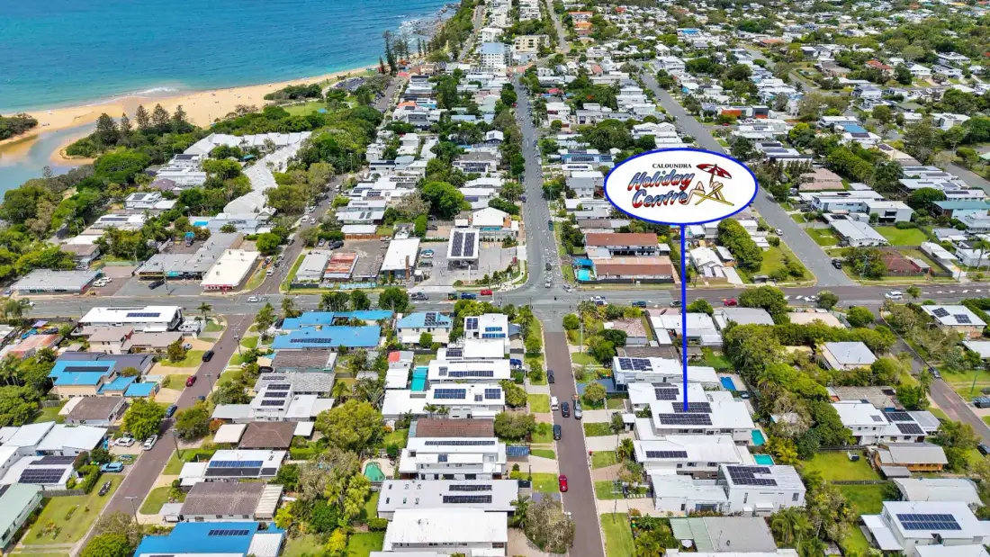 An aerial view shows a coastal neighborhood with homes, streets, and the beach.