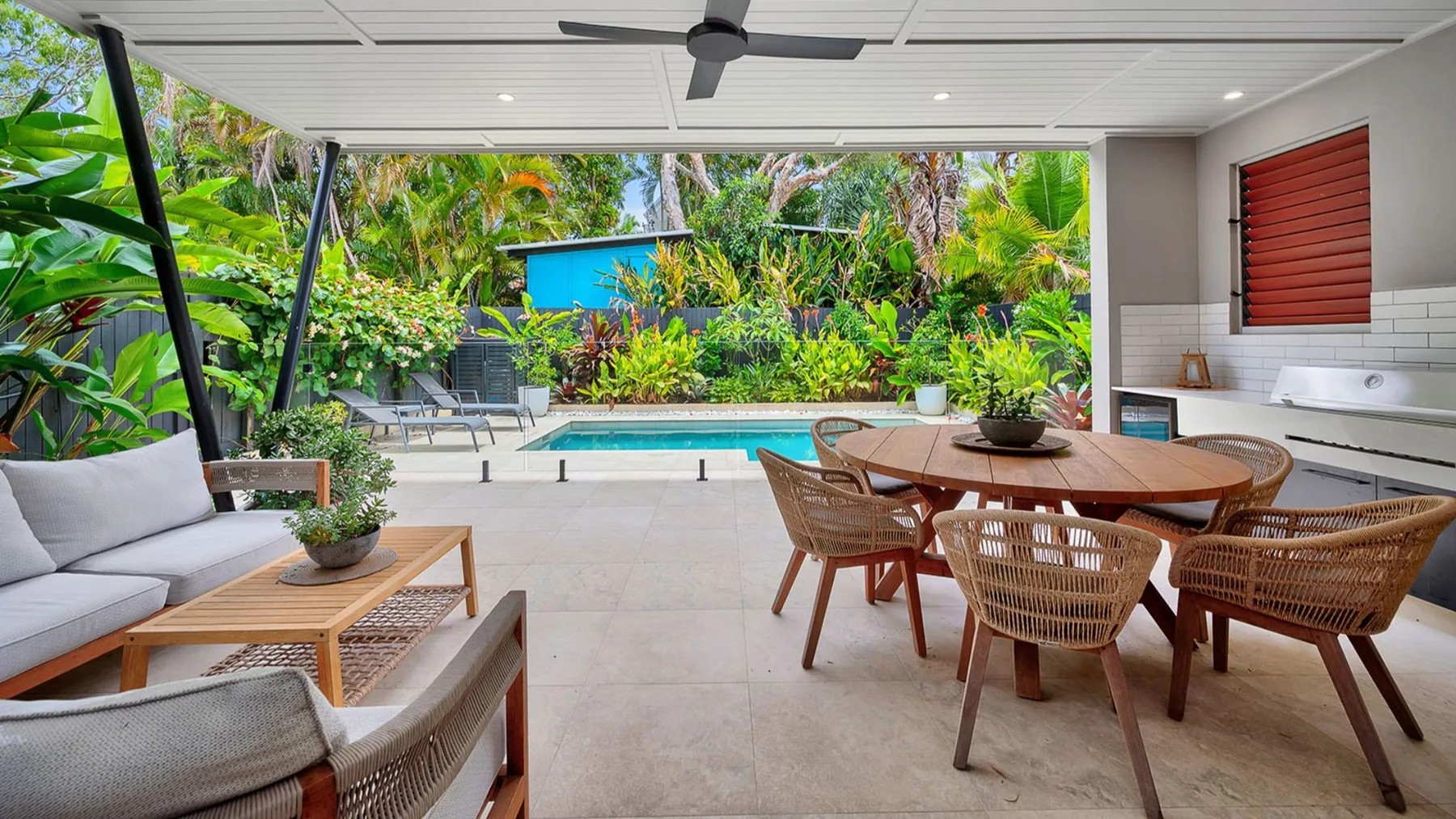 A covered patio with dining and lounge seating overlooks a pool and garden.