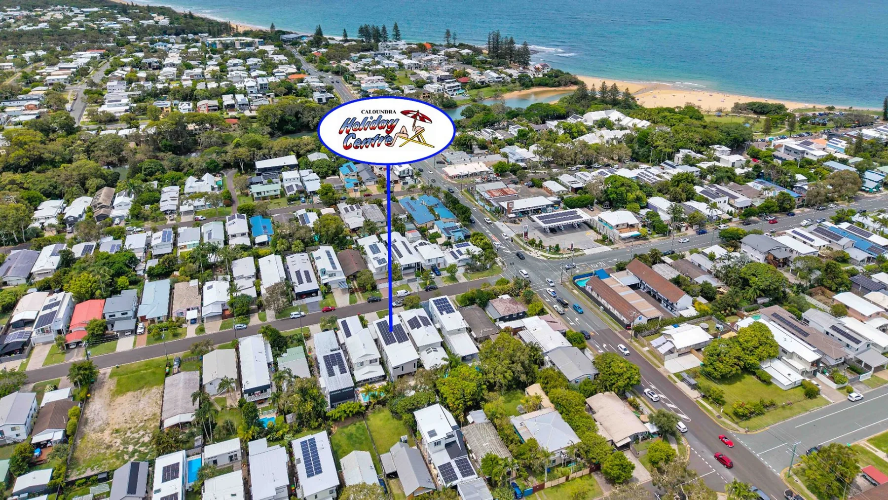 An aerial view shows a coastal neighborhood with homes, roads, and the beach.