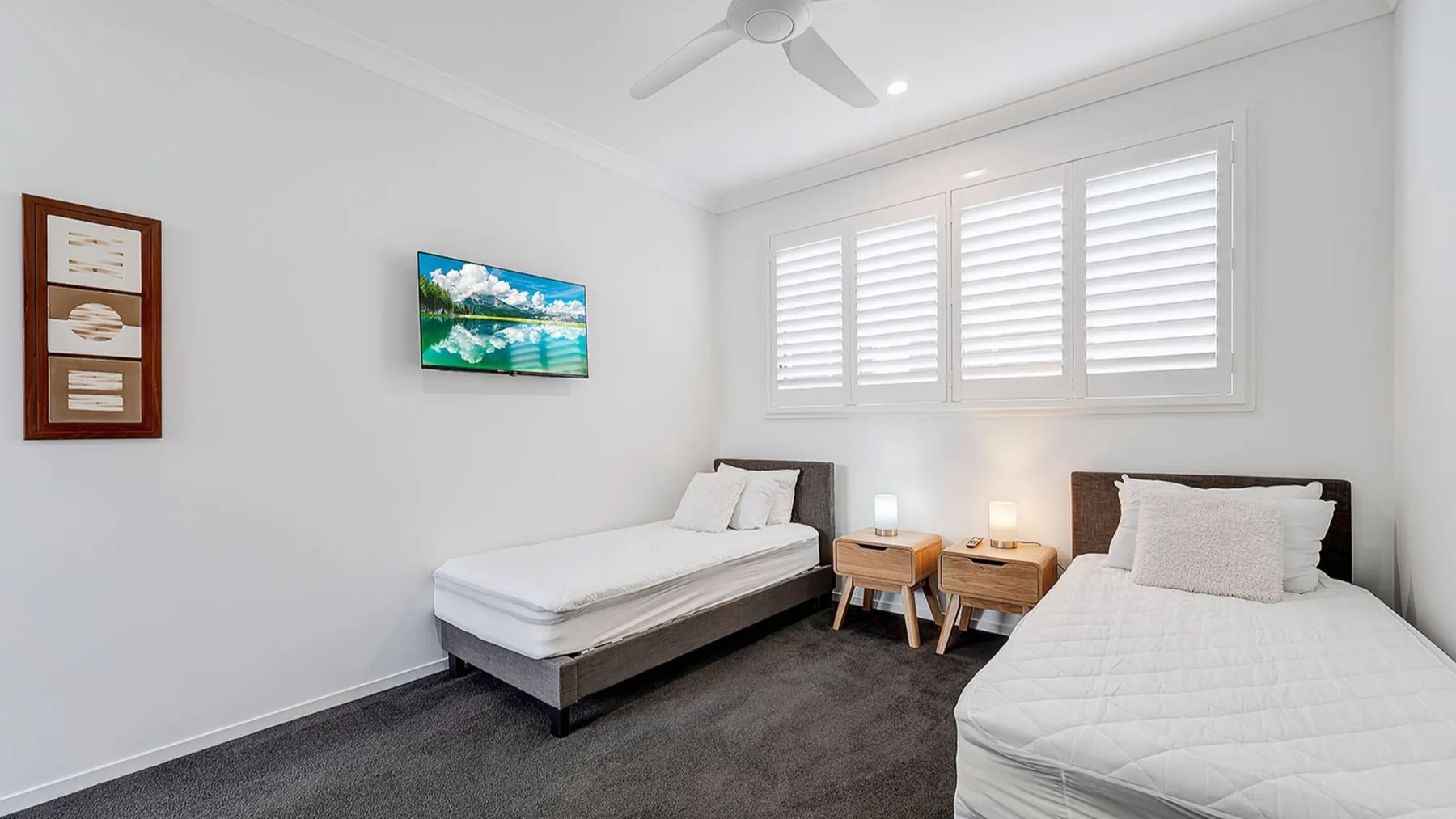 A bright bedroom with two beds, bedside tables, and shuttered windows.