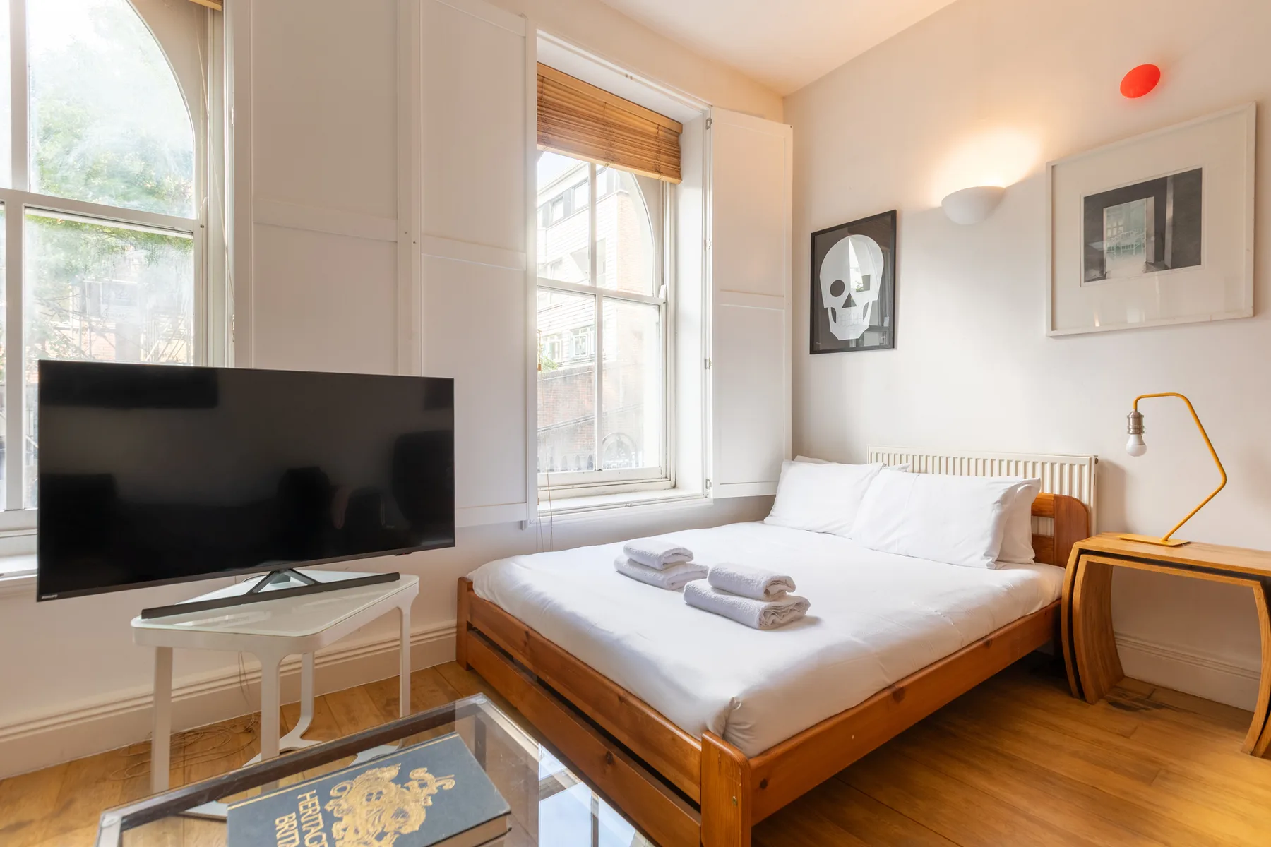 Un dormitorio luminoso con una cama, ventanas grandes y un televisor.