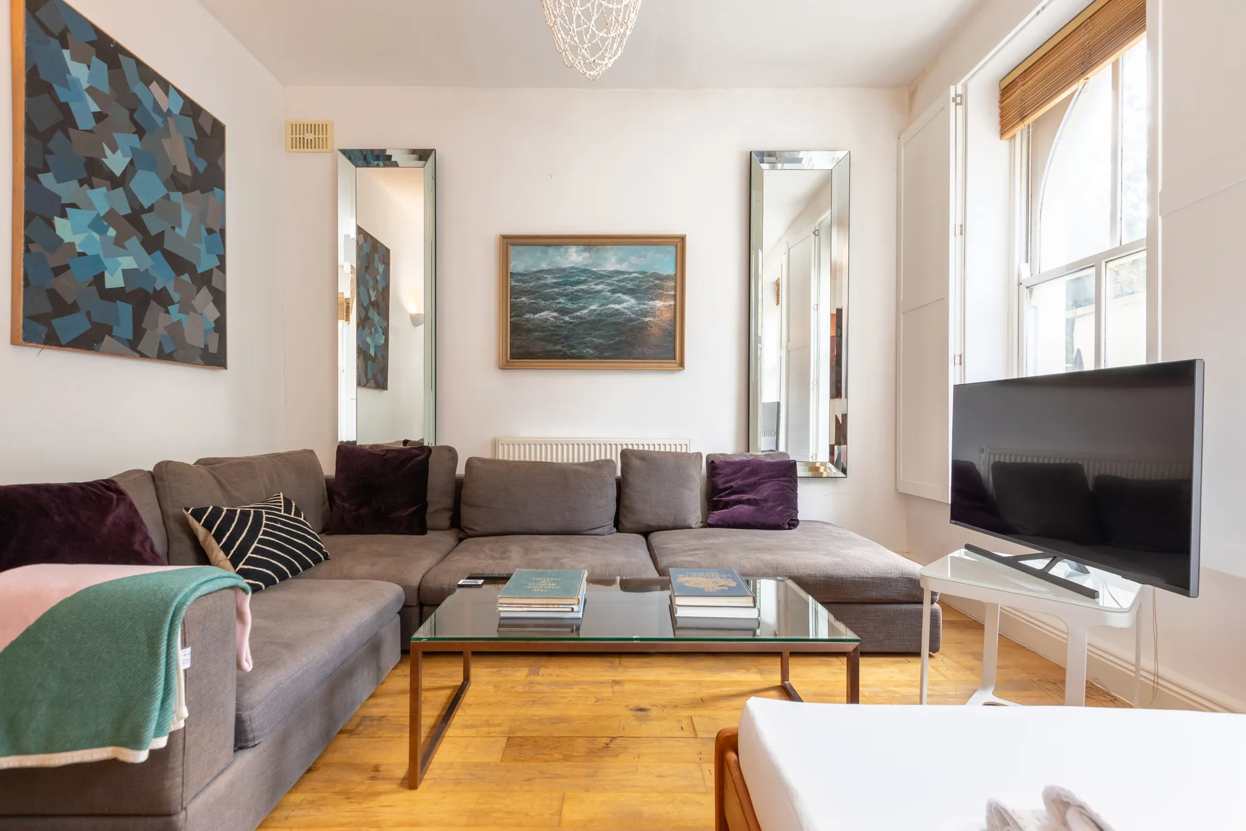 Una sala luminosa tiene asientos seccionales, una mesa de centro de vidrio y un televisor.