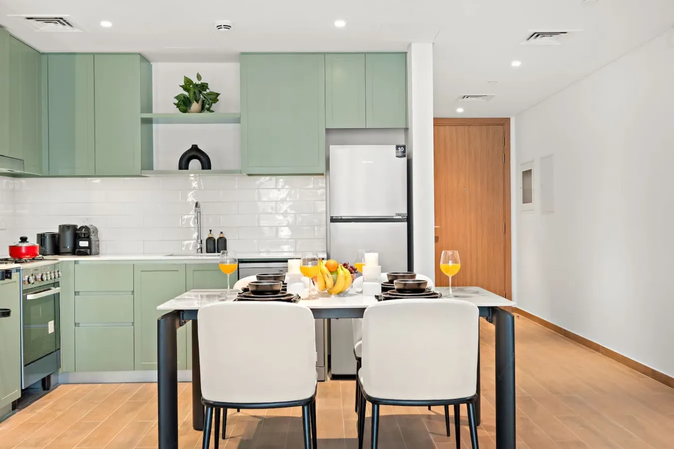 Una cocina y comedor luminosos con gabinetes verdes y una mesa puesta.