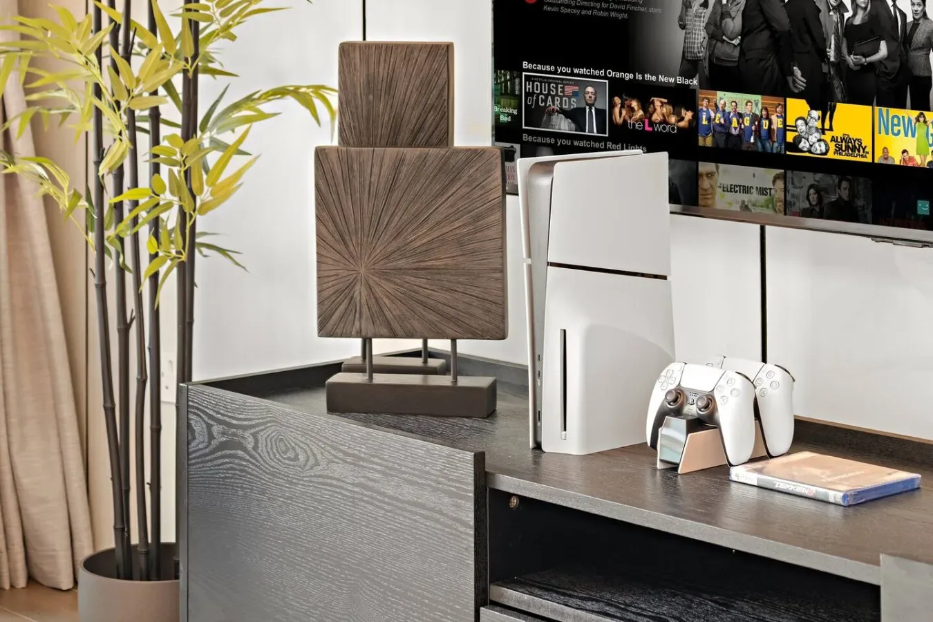 Un mueble de entretenimiento muestra un televisor, una consola de videojuegos, mandos y objetos decorativos.