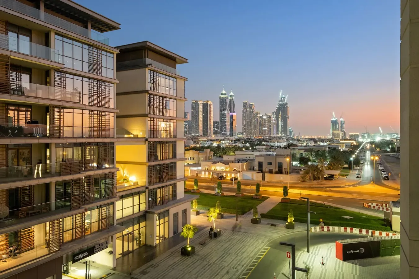 Edificios de apartamentos modernos dan a un horizonte urbano y calles iluminadas al anochecer.