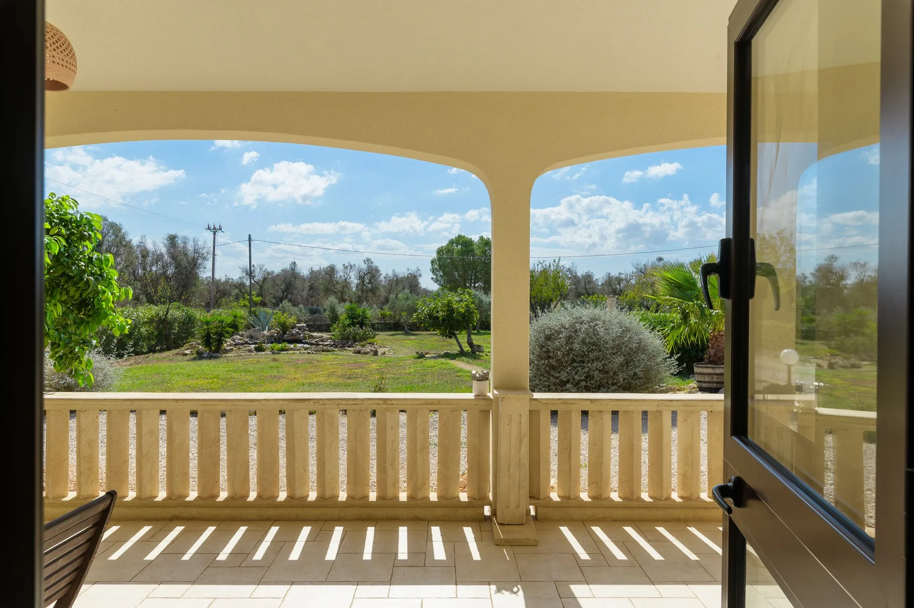 Un patio cubierto da a un jardín ajardinado y tiene una puerta de vidrio abierta.