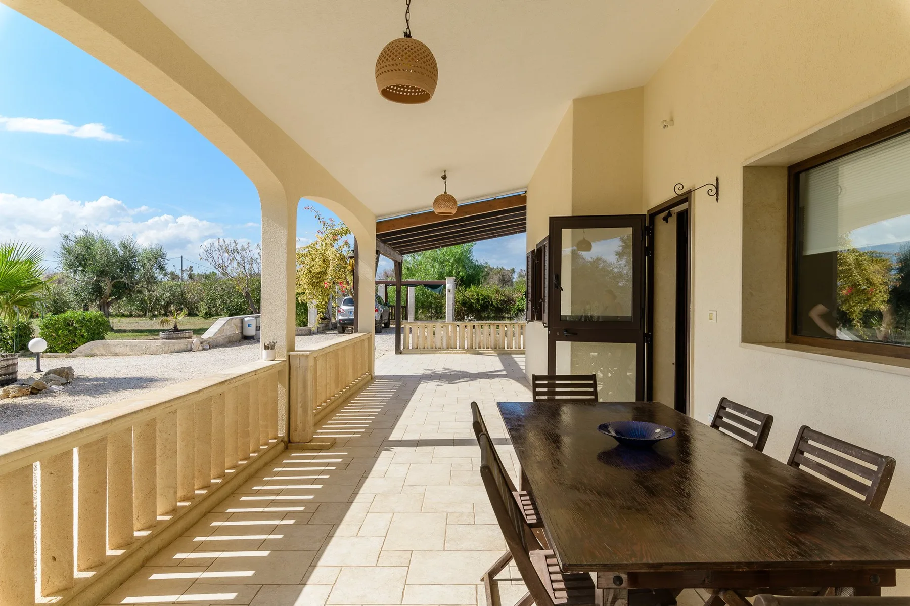 A covered outdoor dining area with a table and chairs beside an open garden view.