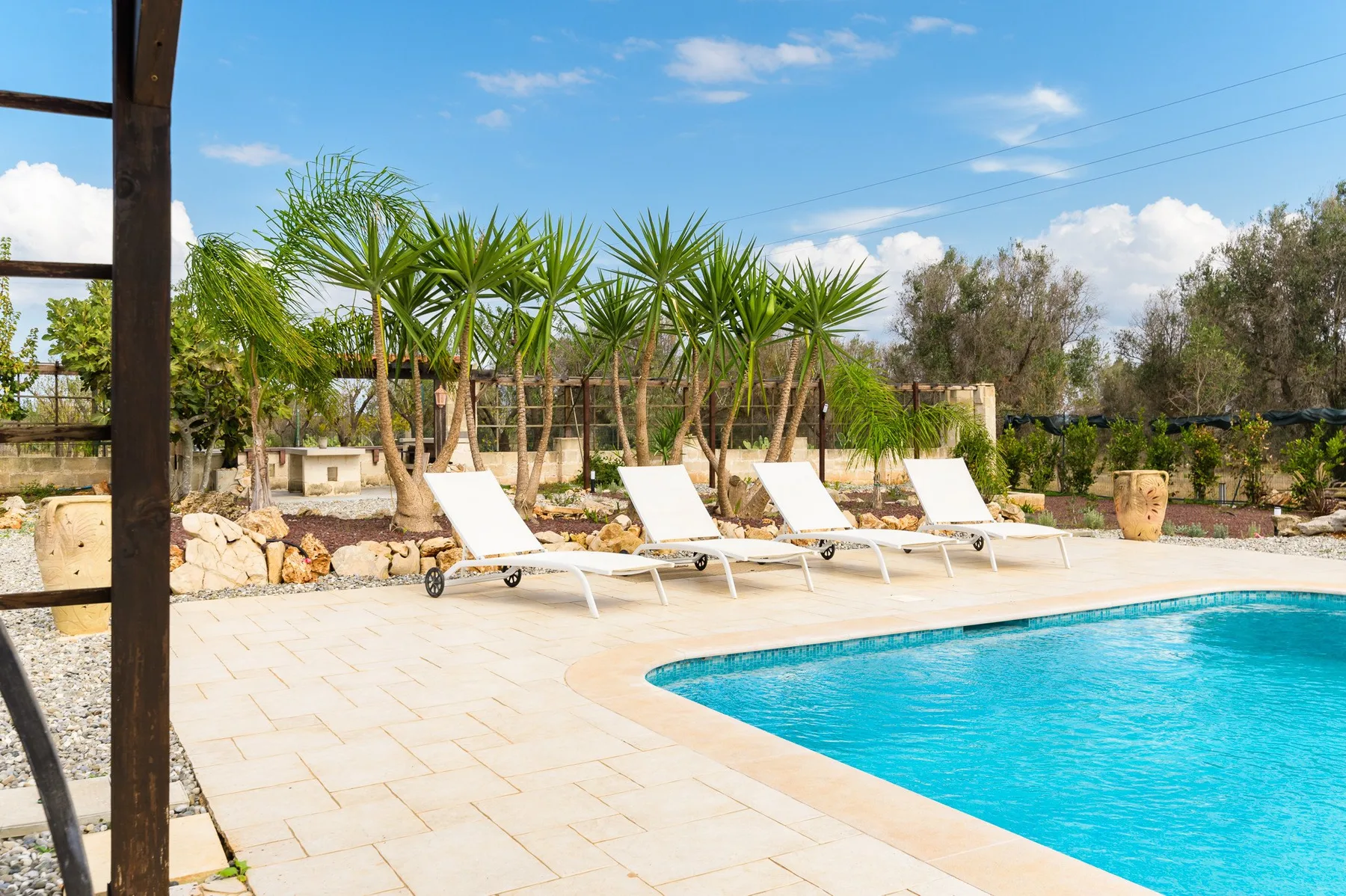 Una piscina al aire libre con asientos reclinables y palmeras en un jardín ajardinado.